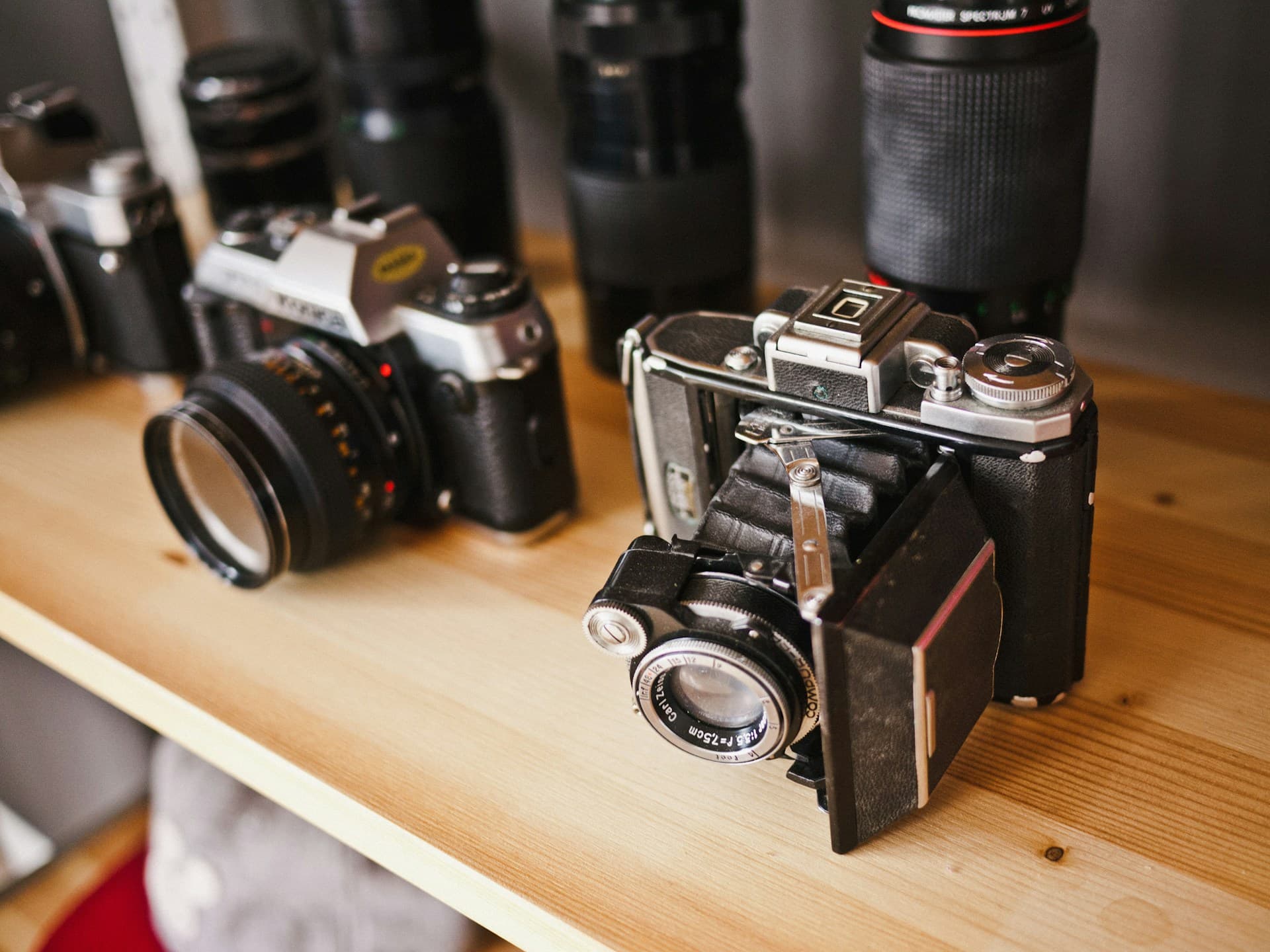 Two black analog film cameras sit side by side on a wooden surface
